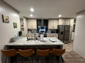 Una cocina moderna con una isla central, taburetes de bar y un refrigerador de acero inoxidable.