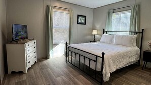 Een slaapkamer met een bed, een dressoir, een televisie en een raam met gordijnen.