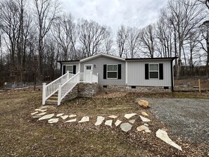 A two-story house with a stone pathway leading to the front door, surrounded by a wooded area.