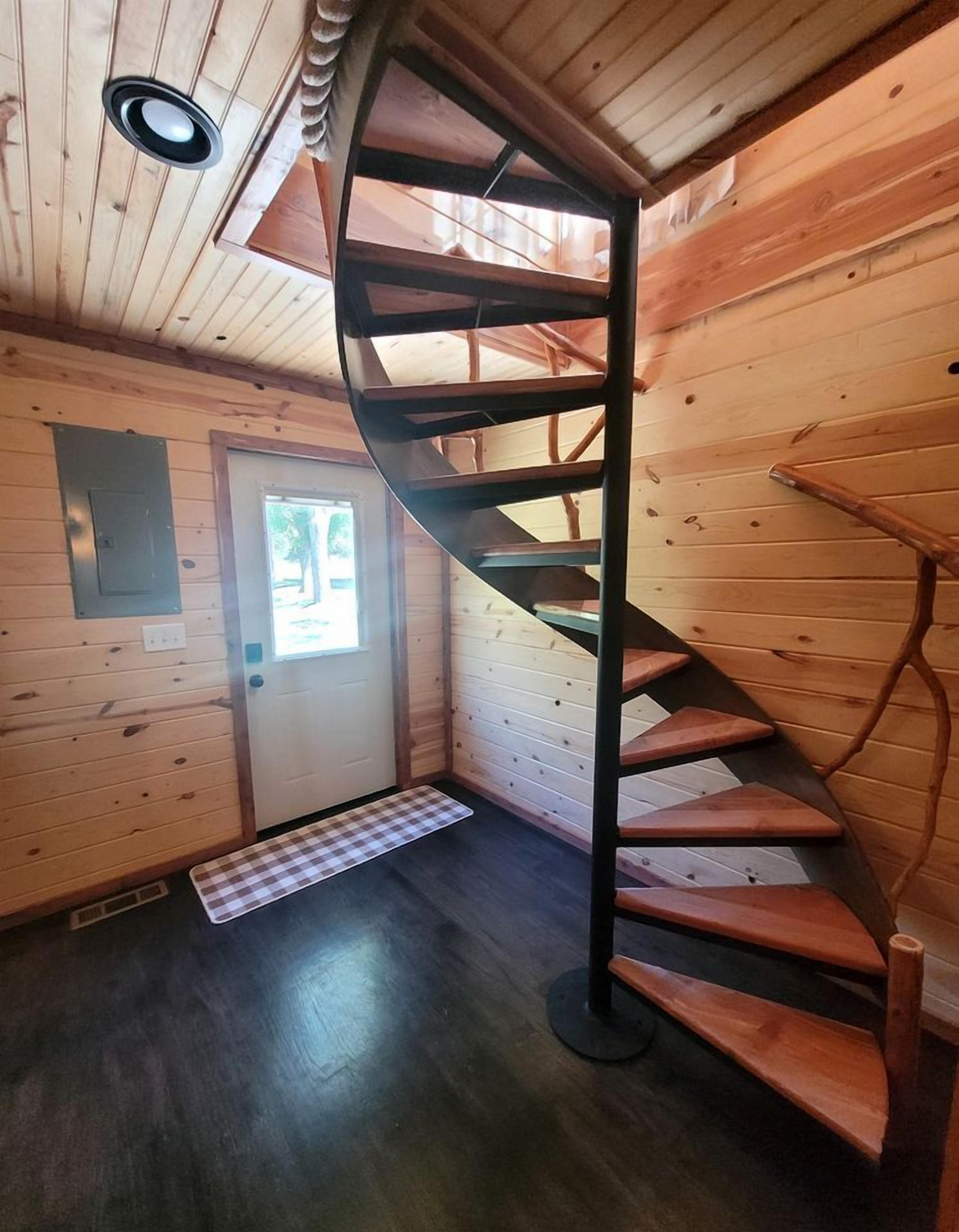 A spiral staircase in a wooden interior with a door and a small mat at the base.