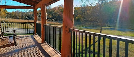 A wooden deck with a railing, a bench, and a view of a grassy field and trees.