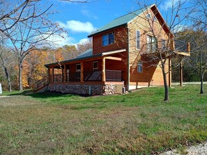 Eine zweistöckige Blockhütte mit Steinunterbau, einer Veranda mit Geländern und einer sichtbaren Treppe, die zum oberen Stockwerk führt.