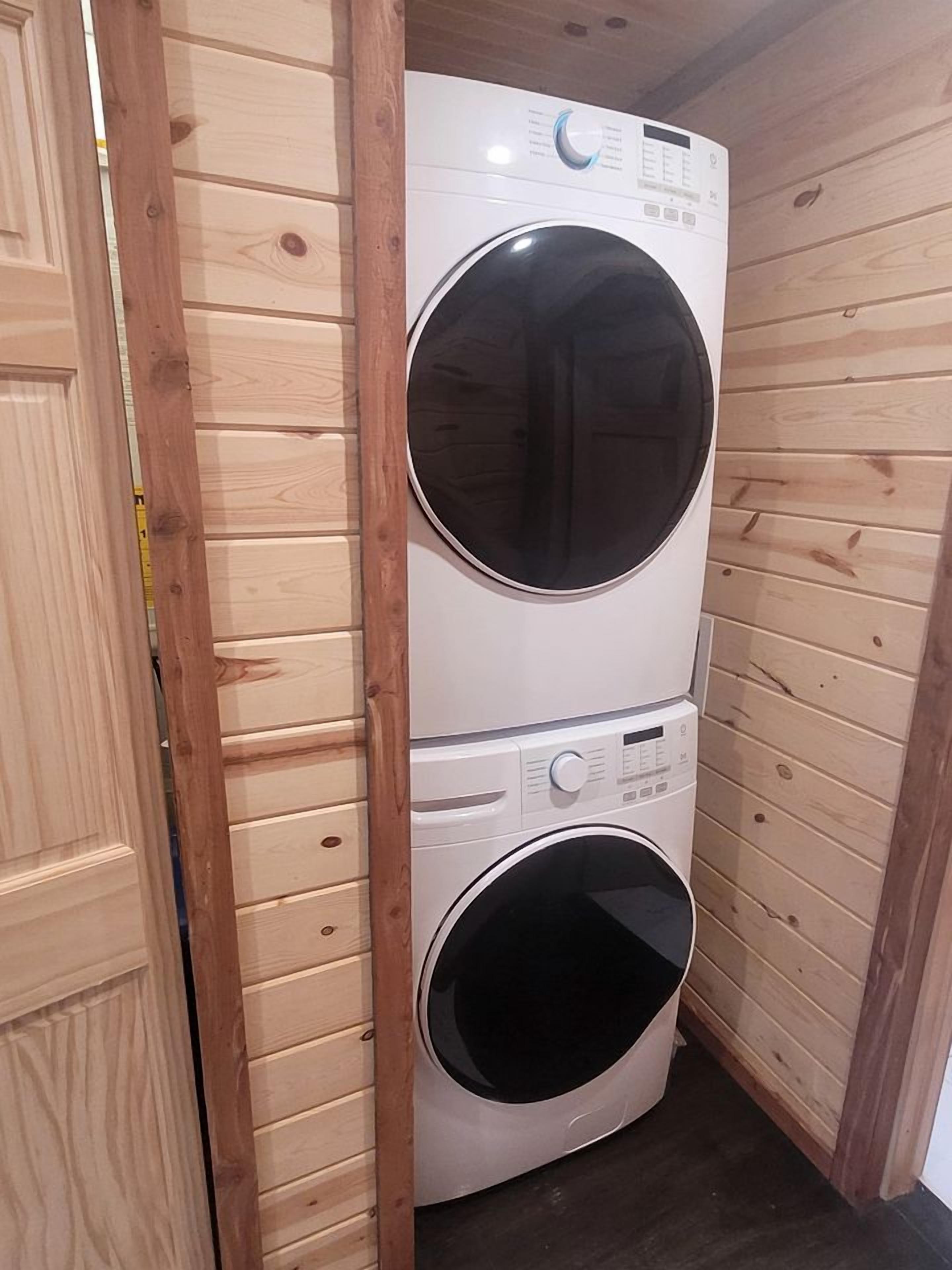 Une machine à laver et un sèche-linge superposés dans une buanderie dont les murs sont en bois.