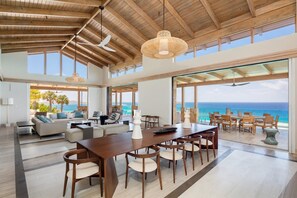 A spacious living area with a large wooden ceiling, a dining table, and a view of the ocean.