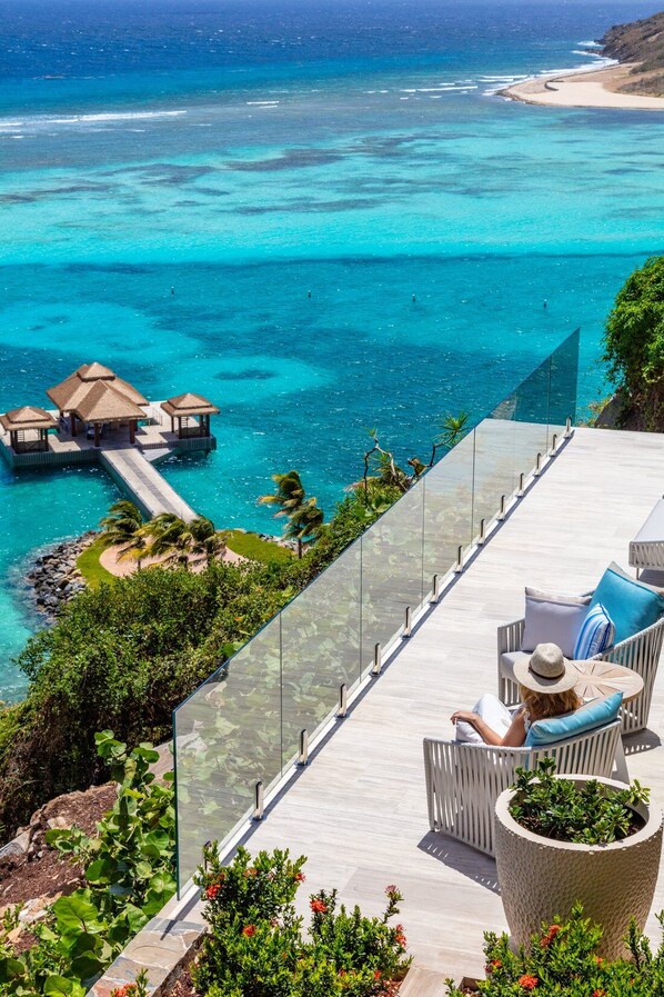 A resort with a glass balustrade, outdoor seating, and a view of the ocean.