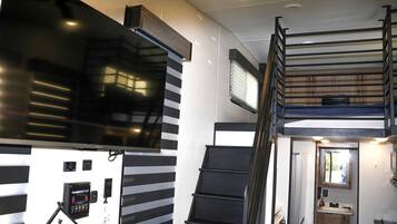 A compact interior with a staircase, a mounted television, and a control panel.