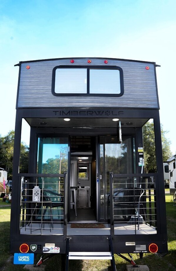 A black recreational vehicle with a 'Timberwolf' logo, a sliding door entrance, and a small porch area with seating.