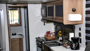 Una kitchenette compacta con estufa, microondas y un lavamanos pequeño.