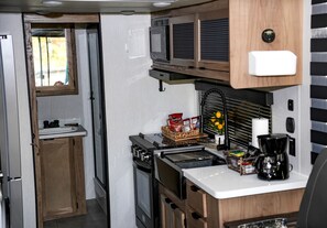 Una kitchenette compacta con estufa, microondas y un lavamanos pequeño.