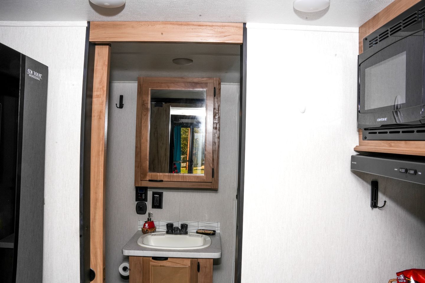 A compact bathroom with a wooden-framed mirror, a sink, and a microwave.