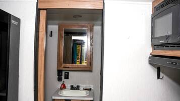 A compact bathroom with a wooden-framed mirror, a sink, and a microwave.