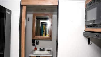 A compact bathroom with a wooden-framed mirror, a sink, and a microwave.