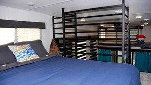 Una cama litera con colchón azul, un almohadón con diseño de ola y una escalera de madera.