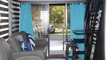 Een kamer met een schuifdeur naar een terras, een grijze bank met een kussen en een kleine tafel.
