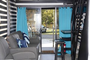 A room with a sliding glass door to a patio, a grey sofa with a pillow, and a small table.