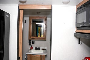 A compact bathroom with a wooden-framed mirror, a sink, and a microwave.