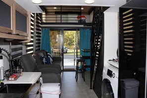 Ein kompaktes Wohnmobil-Interieur mit einer Küchenzeile, einer Sitzecke und einem Fenster mit Blick auf einen Garten.