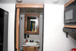 Un baño pequeño con un espejo de marco de madera, un lavamanos y un microondas.