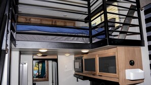 Interior compacto de una caravana con una litera, kitchenette y un baño pequeño.