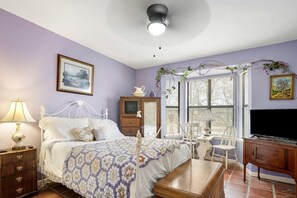 A bedroom with a bed, bedside table, dresser, TV, and a window with blinds. - Riverbank Escape for Families and Friends with Ping Pong, Mrs. Pac-Man, and Cozy Den in Kerrville, Texas (Kerrville)