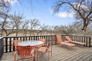 A wooden deck with a glass table and orange wicker chairs. - Riverbank Escape for Families and Friends with Ping Pong, Mrs. Pac-Man, and Cozy Den in Kerrville, Texas (Kerrville)