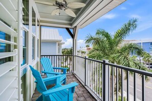 Ein Balkon mit zwei blauen StĂŒhlen, einem Deckenventilator und Blick auf Palmen und GebĂ€ude.