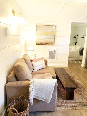 Un salon chaleureux avec un canapé, un banc, une lampe fixée au mur, un tableau et une petite table.