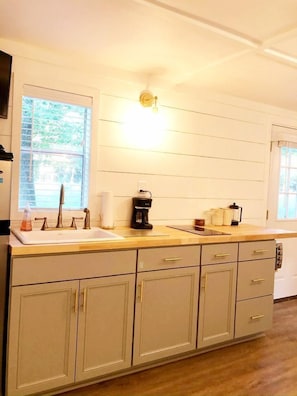 A kitchen with a sink, countertop, cabinets, and a window with blinds.