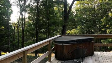 Eine Holzterrasse mit Whirlpool und zwei Stühlen, umgeben von Bäumen.