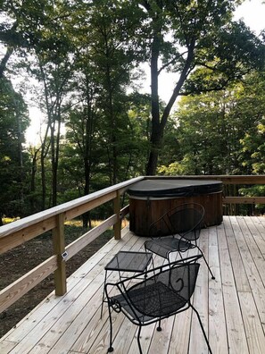 Une terrasse en bois avec un jacuzzi et deux chaises, entourée d’arbres.