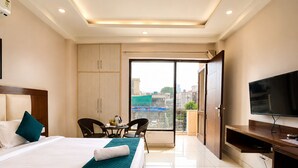 A hotel room with a bed, a TV, a desk, a chair, a balcony with a view, and a wardrobe. - The Milford Noida (Noida)