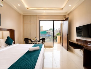 A hotel room with a bed, a TV, a desk, a chair, a balcony with a view, and a wardrobe.