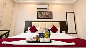 A hotel room with a bed, a tray with breakfast items, a painting on the wall, and an air conditioning unit. - The Milford Noida (Noida)