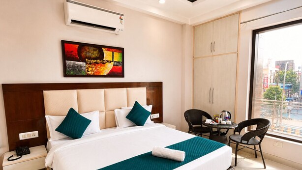 A hotel room with a bed, bedside table, chair, and a view of the city. - The Milford Noida (Noida)