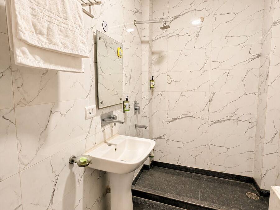 A bathroom with a white marble wall, a pedestal sink, a handheld showerhead, and a towel rack.