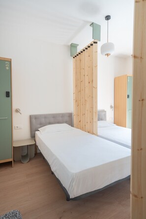 Quarto de hotel com duas camas, um divisória de madeira, um pequeno espaço para sentar e um guarda-roupa.