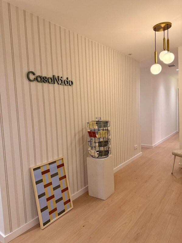 A hallway with a striped wall, a framed artwork, a display of postcards, and a hanging light fixture.