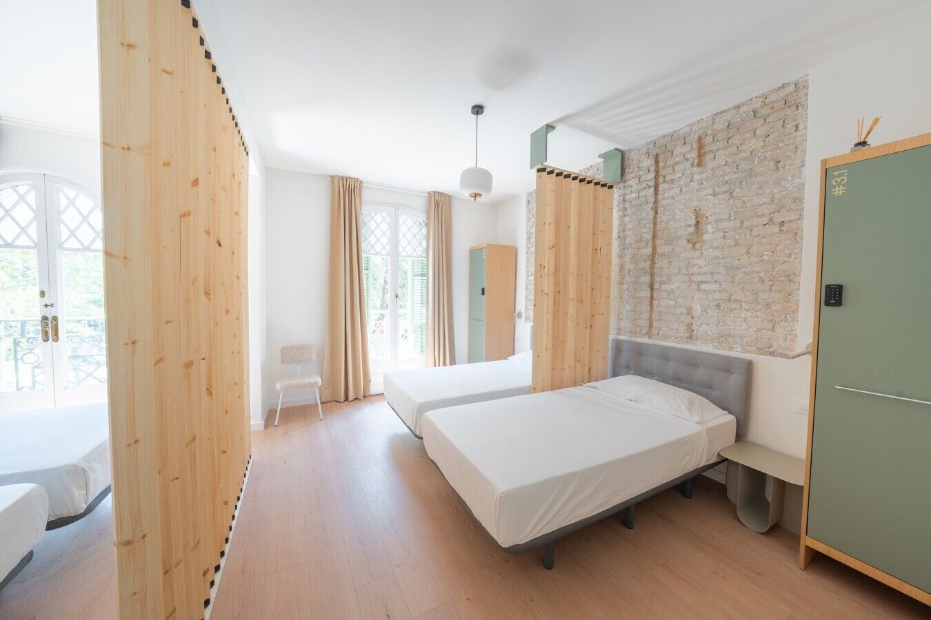A room with two beds, a wooden wardrobe, a green door, and a brick wall.