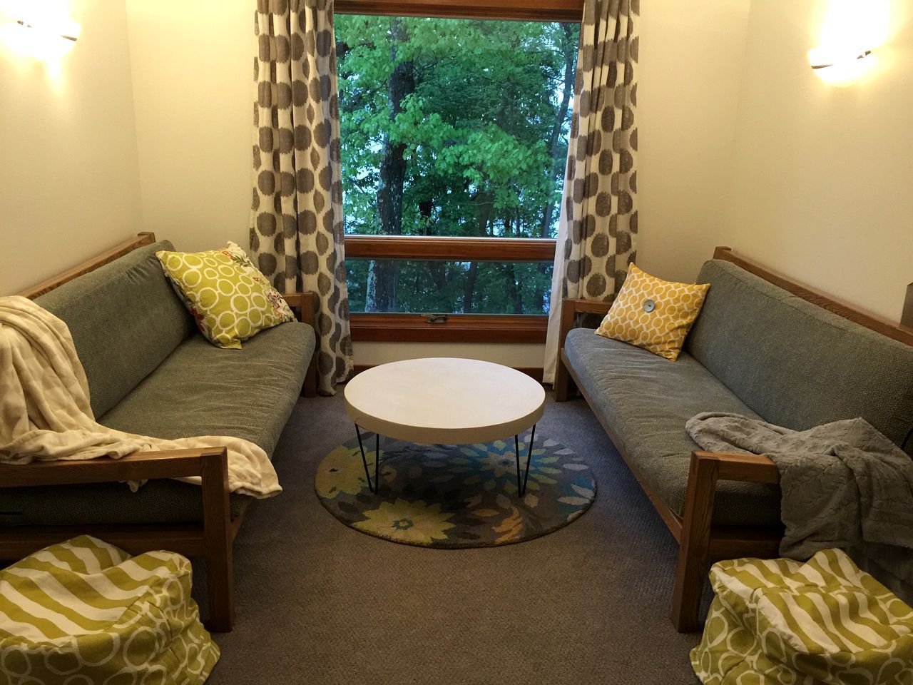 Una sala de estar acogedora con dos sofás, una mesa de centro redonda y vistas a árboles a través de una ventana.