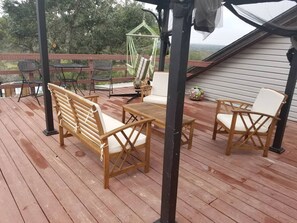 Una terraza de madera con mobiliario exterior, incluyendo un banco, dos sillas y una mesa.