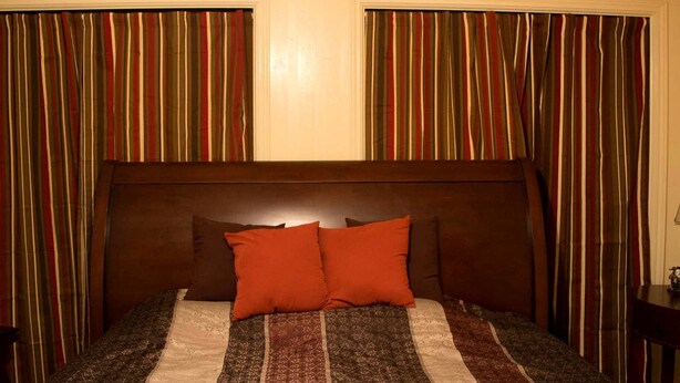 A hotel room with a large bed, striped curtains, and a headboard. - Idyllic Cottage Rental Perfect for an Outdoor Getaway in Killeen, Texas (Killeen)