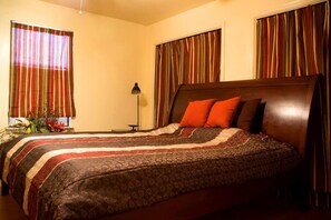 Habitación de hotel con una cama grande, cortinas a rayas, una mesita de noche y una lámpara.