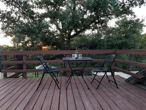 A wooden deck with a table and two chairs, surrounded by a metal fence.