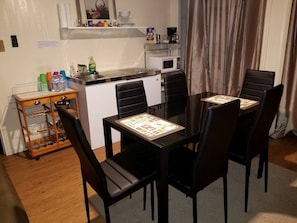 A dining area with a table and chairs, a kitchen in the background, and a small cabinet with bottles.