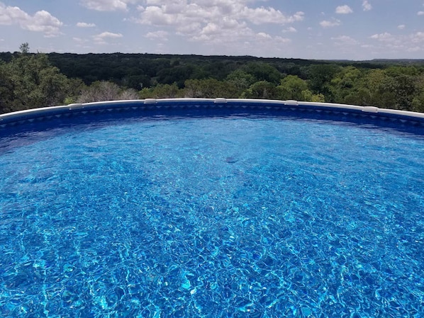 A clear blue swimming pool with a view of a forested landscape.