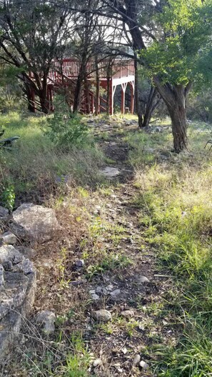 Un sendero que lleva a una estructura roja con arcos blancos, rodeada de árboles y césped.