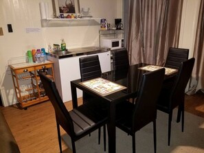 Un comedor con una mesa y sillas, una cocina al fondo y un mueble bajo con botellas.