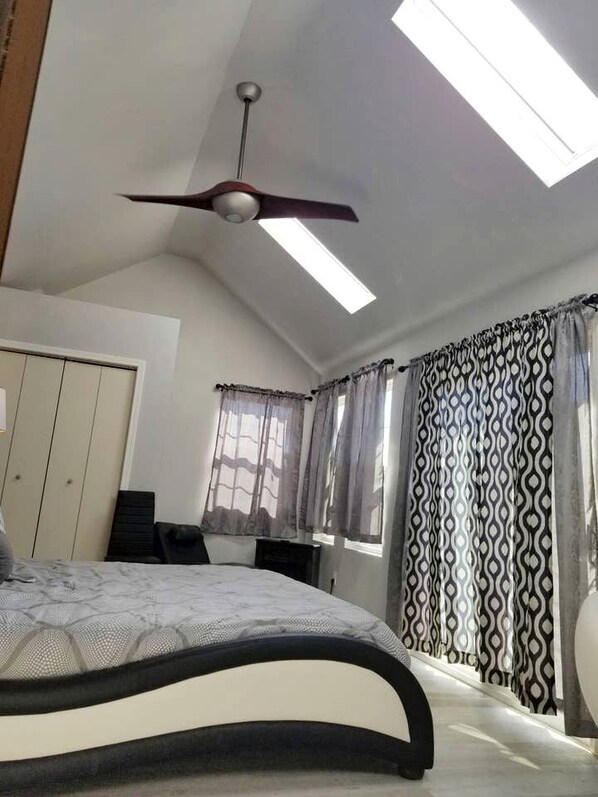Un dormitorio con cama, ventilador de techo, armario, escritorio y ventana con cortinas estampadas.