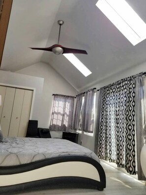 A bedroom with a bed, a ceiling fan, a wardrobe, a desk, and a window with patterned curtains. - Idyllic Cottage Rental Perfect for an Outdoor Getaway in Killeen, Texas (Killeen)