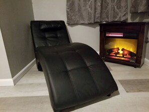 Un otomán de cuero negro, una chimenea y una pared gris.